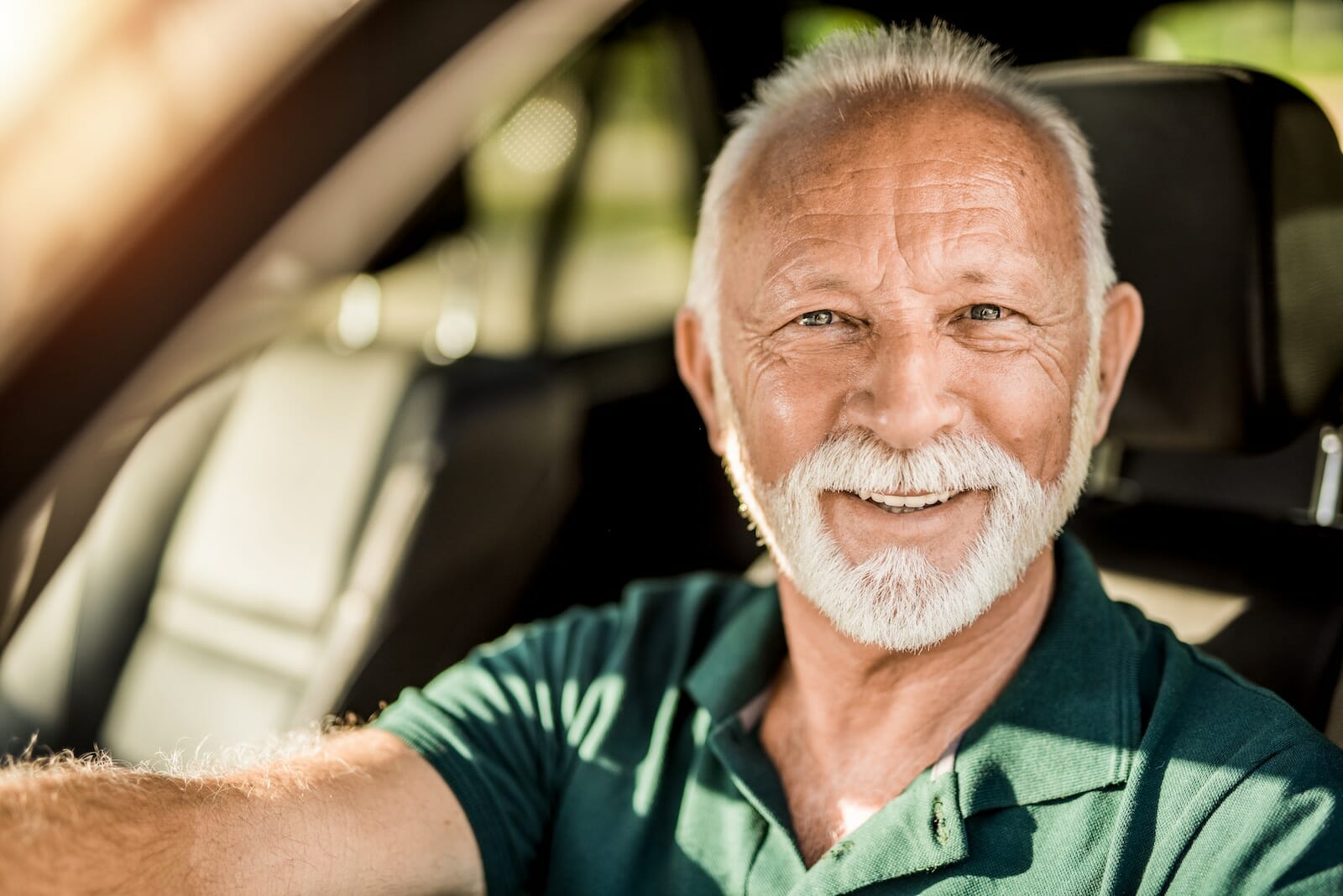 Headshot of happy senior man in his car looking at camera.