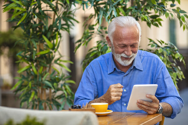 Senior man using a digital tablet. Leisure Lifestyle Relaxation Solitude Technology Concept. Senior man reading news on digital tablet. Successful senior businessman in cafe.